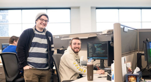 Two developers smiling in a modern office with code on a monitor